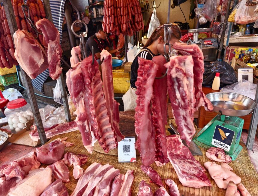 authentic wet market scene in Southeast Asia, Phnom Penh, Cambodia, featuring an array of fresh raw meats on display. The market stall primarily sells various cuts of pork. Prăbușire pe piața cărnii de porc: fermierii români vând sub costul de producție